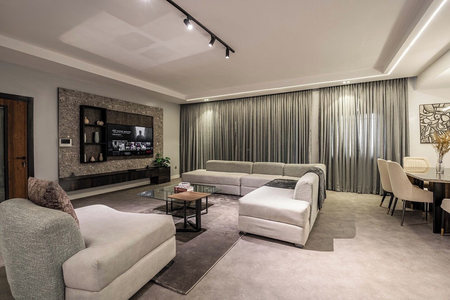A modern living room with a sectional sofa, a glass coffee table, and a flat-screen TV mounted on a stone wall.