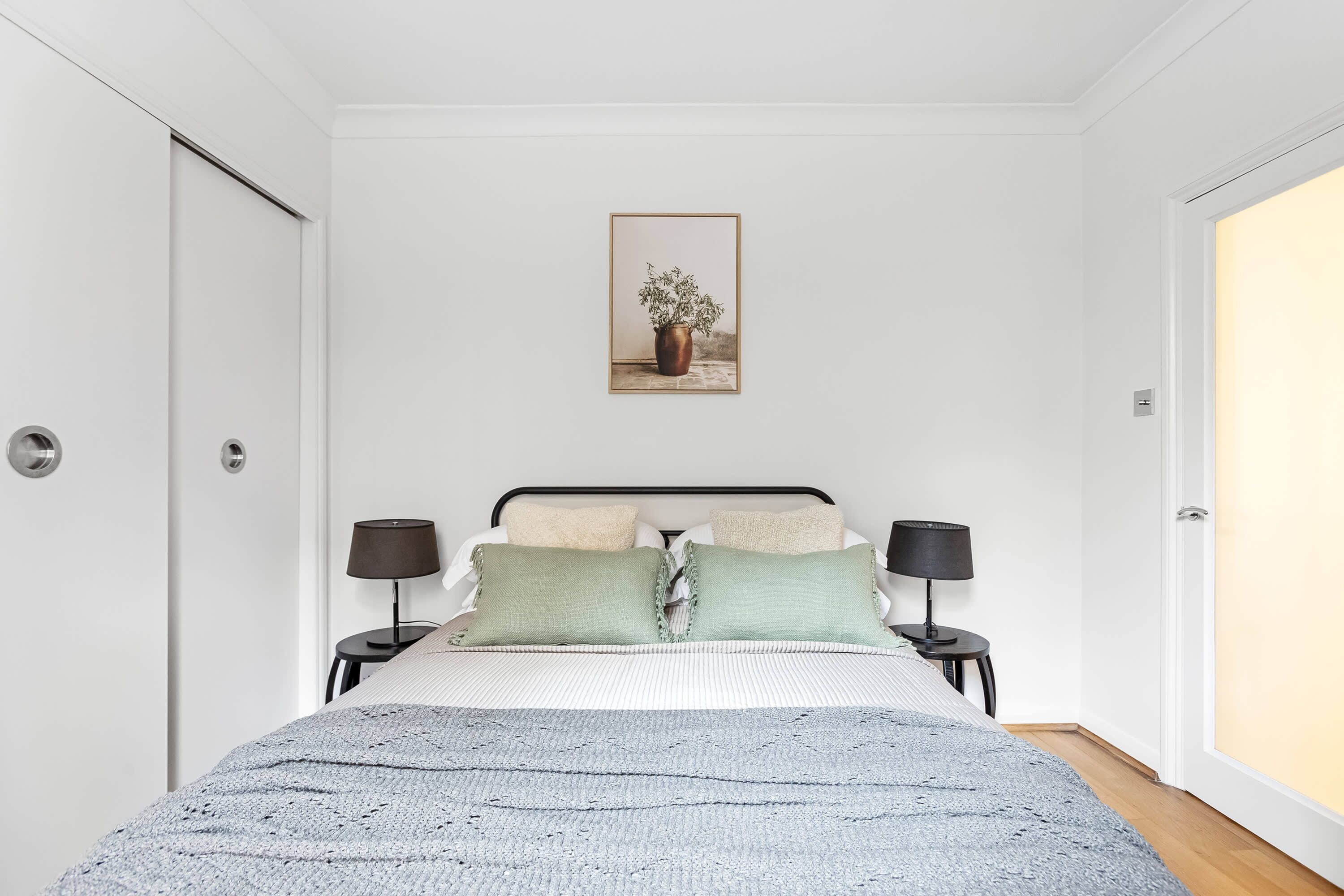 A bedroom with a bed, two bedside tables with lamps, a framed picture on the wall, and a door.