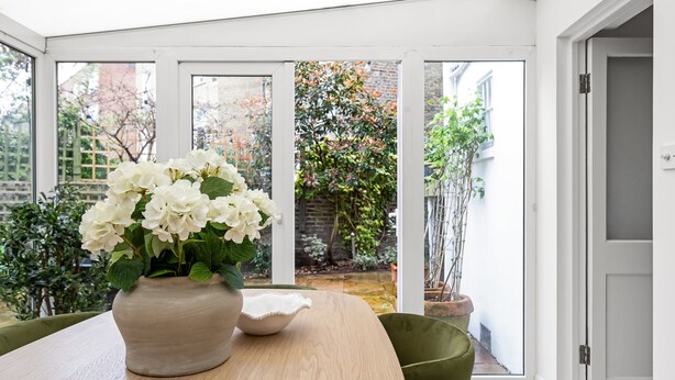 Ein Wintergarten mit Tisch, Stühlen, einem Blumenstrauß und Blick auf den Garten.