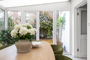 A conservatory with a table, chairs, a vase of flowers, and a view of the garden. - Stylish 2 Bed 2 Bath - Private Garden (Greater London)