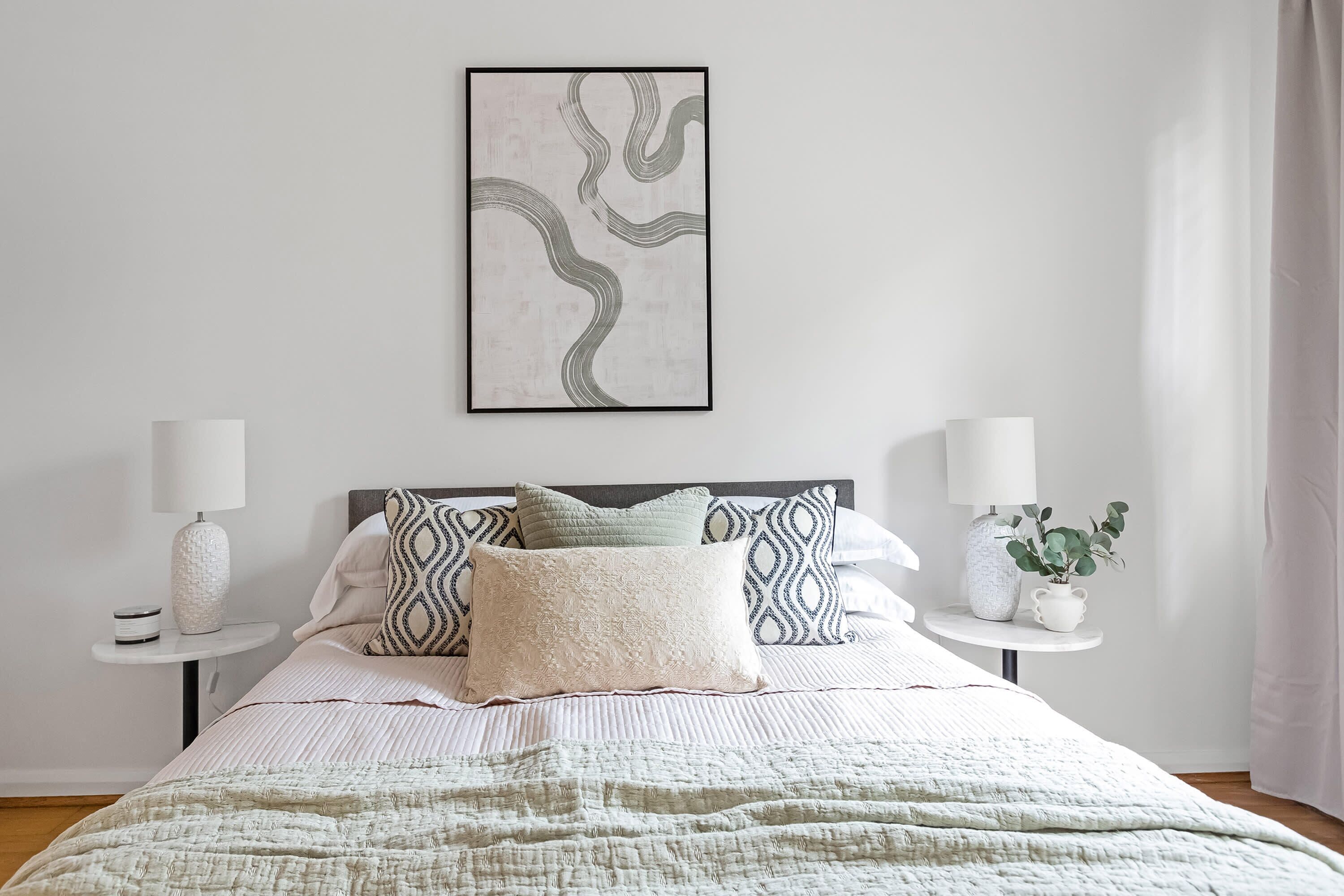 A neatly made bed with a patterned bedspread, two bedside tables with lamps, and a framed abstract artwork on the wall.