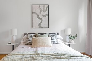 A neatly made bed with a patterned bedspread, two bedside tables with lamps, and a framed abstract artwork on the wall. - Stylish 2 Bed 2 Bath - Private Garden (Greater London)