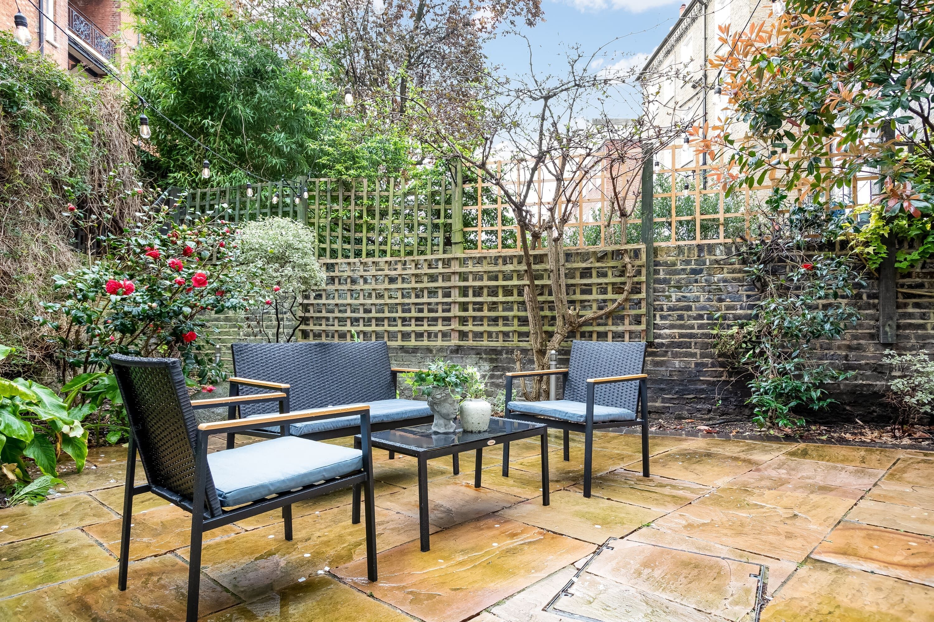 Une terrasse avec une table et des chaises, entourée de plantes et d’une clôture en bois.