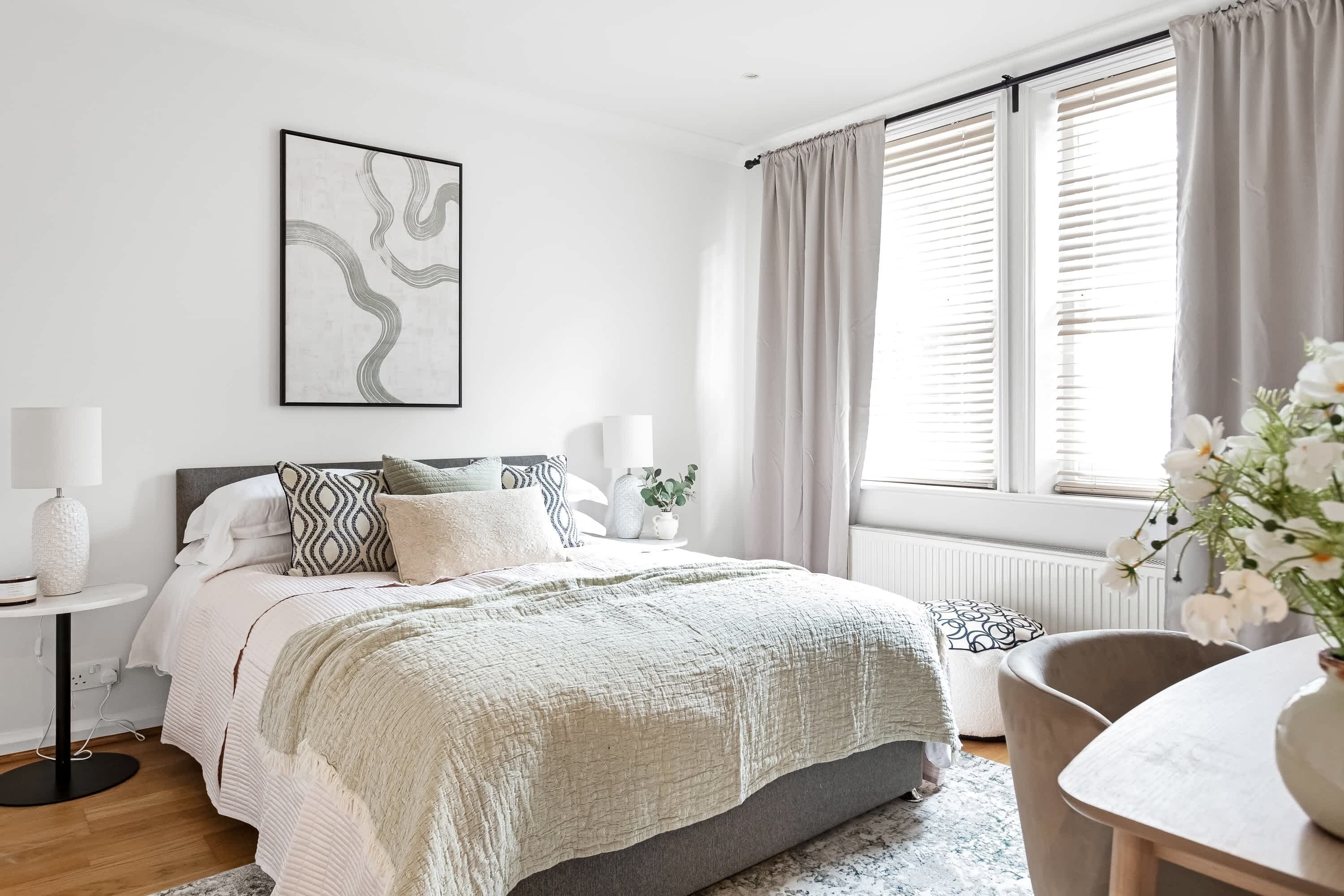 A bedroom with a bed, bedside tables, a window with curtains, and a wall-mounted picture.