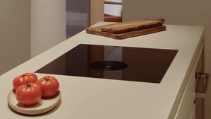 Eine moderne Küche mit eingebautem Kochfeld, einer kleinen Kücheninsel mit Schneidebrett und Brot, und einem Teller mit Tomaten.