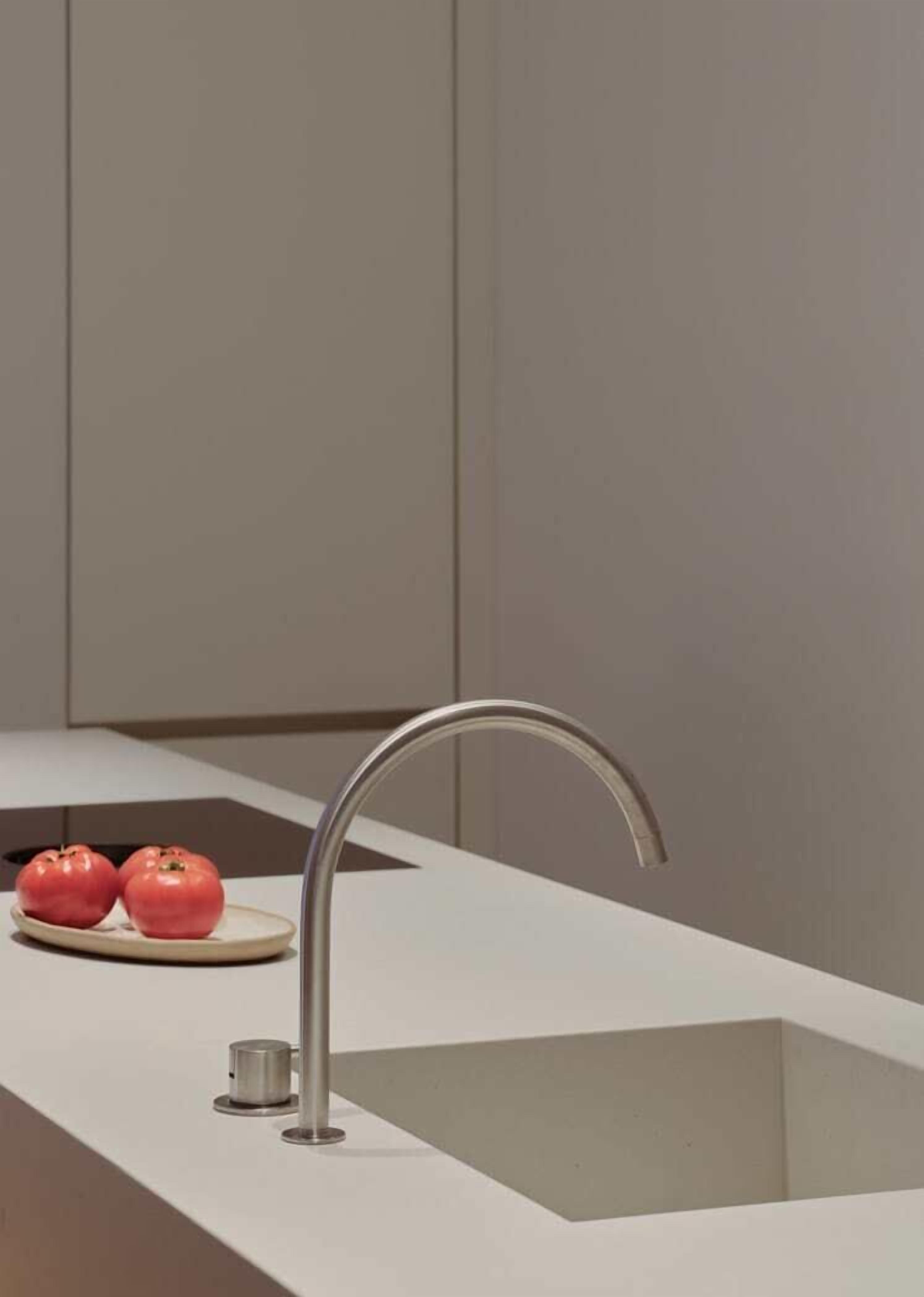A modern kitchen with a stainless steel sink, a white countertop, and two red apples on a plate.
