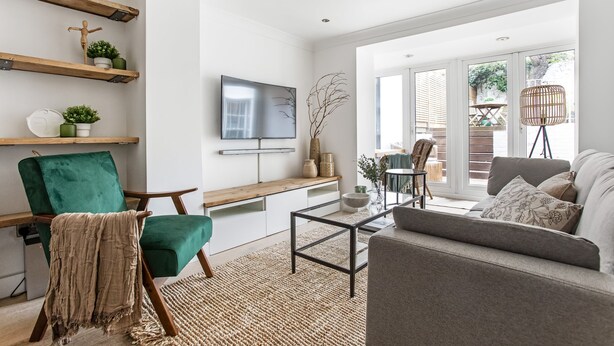 A living room with a green armchair, a grey sofa, a coffee table, and a TV on the wall. - Stunning Kensington Apartment with Private Garden (Greater London)