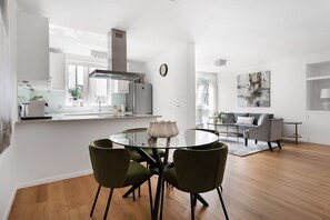 A modern kitchen with a central island, a dining area with a round table and chairs, a grey sofa, and a large abstract painting on the wall. - Notting Hill-Opulent Bright Two Bedroom (Greater London)