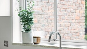 Een keuken met een spoelbak, een raam, een potplant en een bakstenen muur.