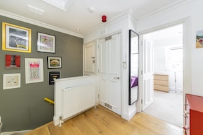 A hallway with a white radiator, a red cabinet, and a door leading to a room with a purple bed. - Notting Hill Bohemian Apartment (London)
