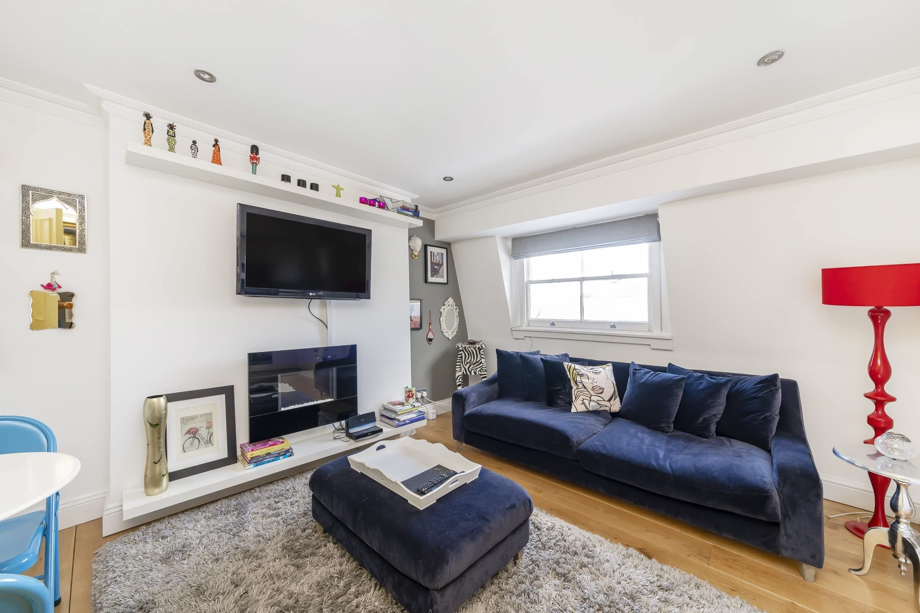 A modern living room with a flat-screen TV, a dark blue sofa, a white coffee table, and a red floor lamp.