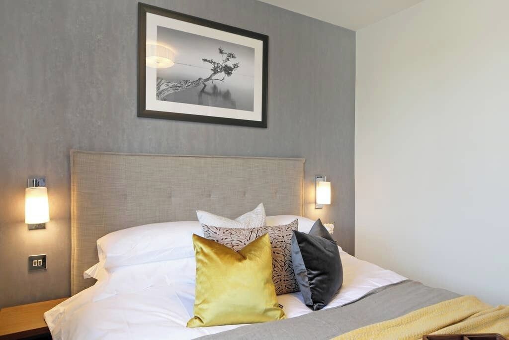A hotel room with a bed, pillows, a framed picture on the wall, and wall-mounted lights.