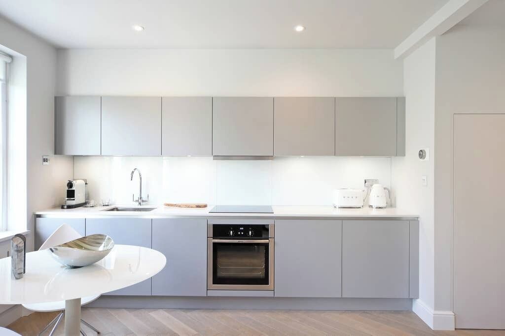 A modern kitchen with grey cabinets, a built-in oven, and a white countertop.