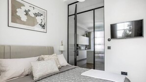 A bedroom with a bed, a TV, a painting, and a sliding door leading to a kitchen.