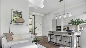 A modern living room with a sofa, ottoman, and a coffee table. There is a kitchen area with a bar and stools.