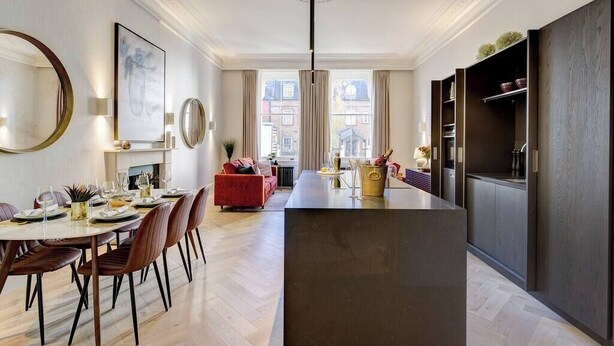 Ein modernes Interieur mit Essbereich, einem roten Sofa und einer Küche mit dunklen Holzschränken.