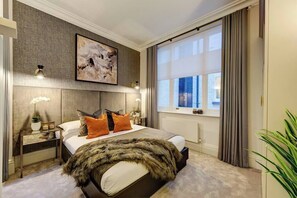 Ein Schlafzimmer mit einem Bett, einem Nachttisch, einer Lampe, einem Gemälde und einem Fenster mit Vorhängen.