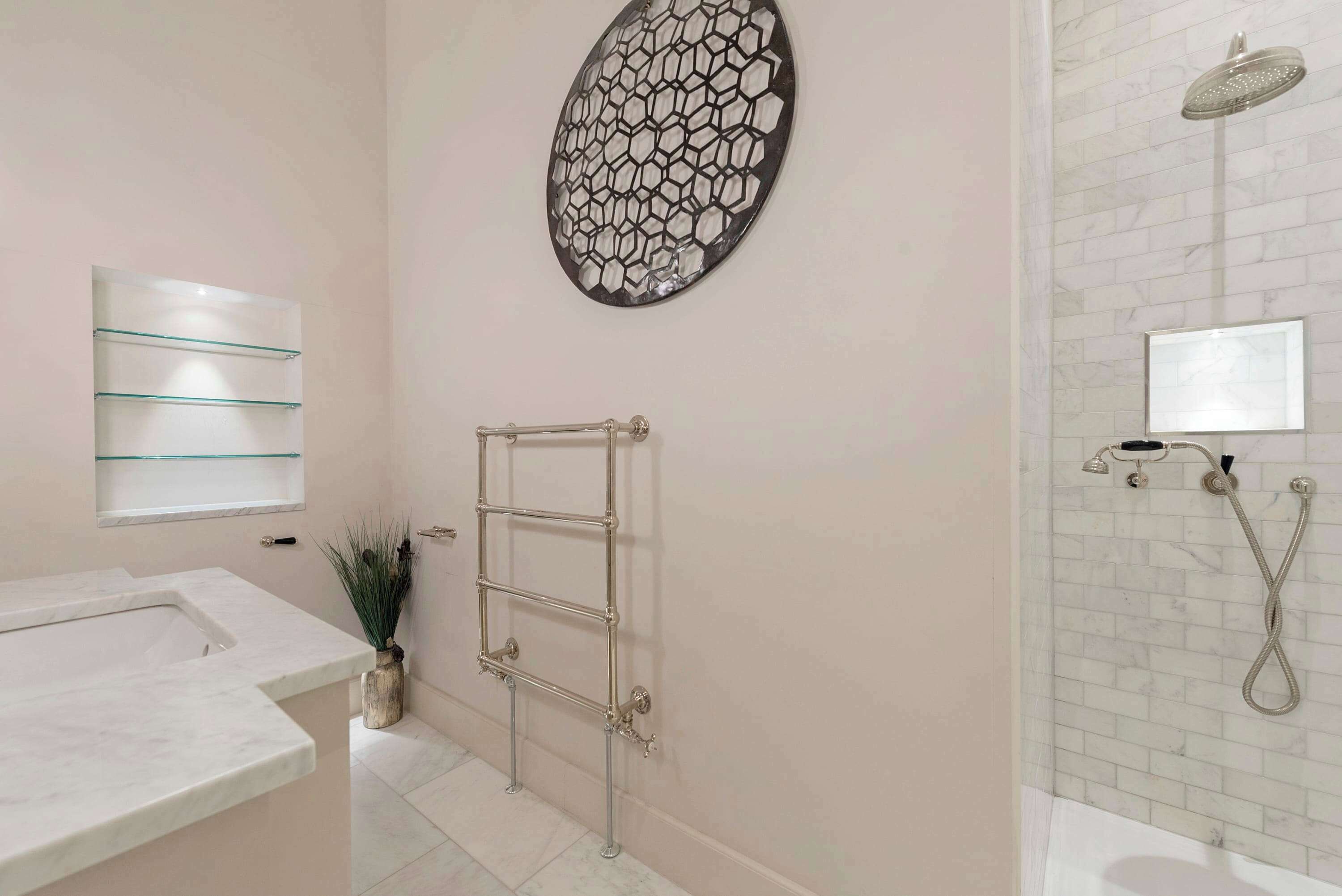 Un bagno con un lavabo in marmo, uno scaffale in vetro, un porta asciugamani, un elemento decorativo a parete e una doccia con soffione manuale.