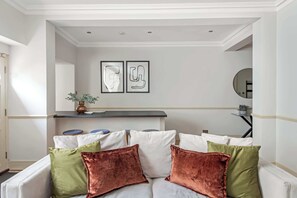 A living room with a white sofa, green and copper cushions, a coffee table, and two framed abstract artworks on the wall. - Notting Hill - Movie Location (London)