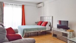 Een slaapkamer met een bed, een televisie, een houten nachtkastje en een raam met gordijnen.