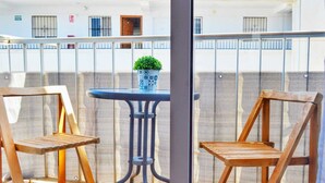 Een balkon met twee houten stoelen, een tafeltje en een bloempot.