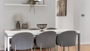 Ett modernt matområde med ett vitt bord, fyra grå stolar, en hängande taklampa och ett trägolv.