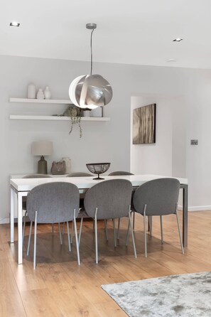 A modern dining area with a white table, four grey chairs, a hanging pendant light, and a wooden floor. - Large Notting Hill Flat with Garden (Greater London)