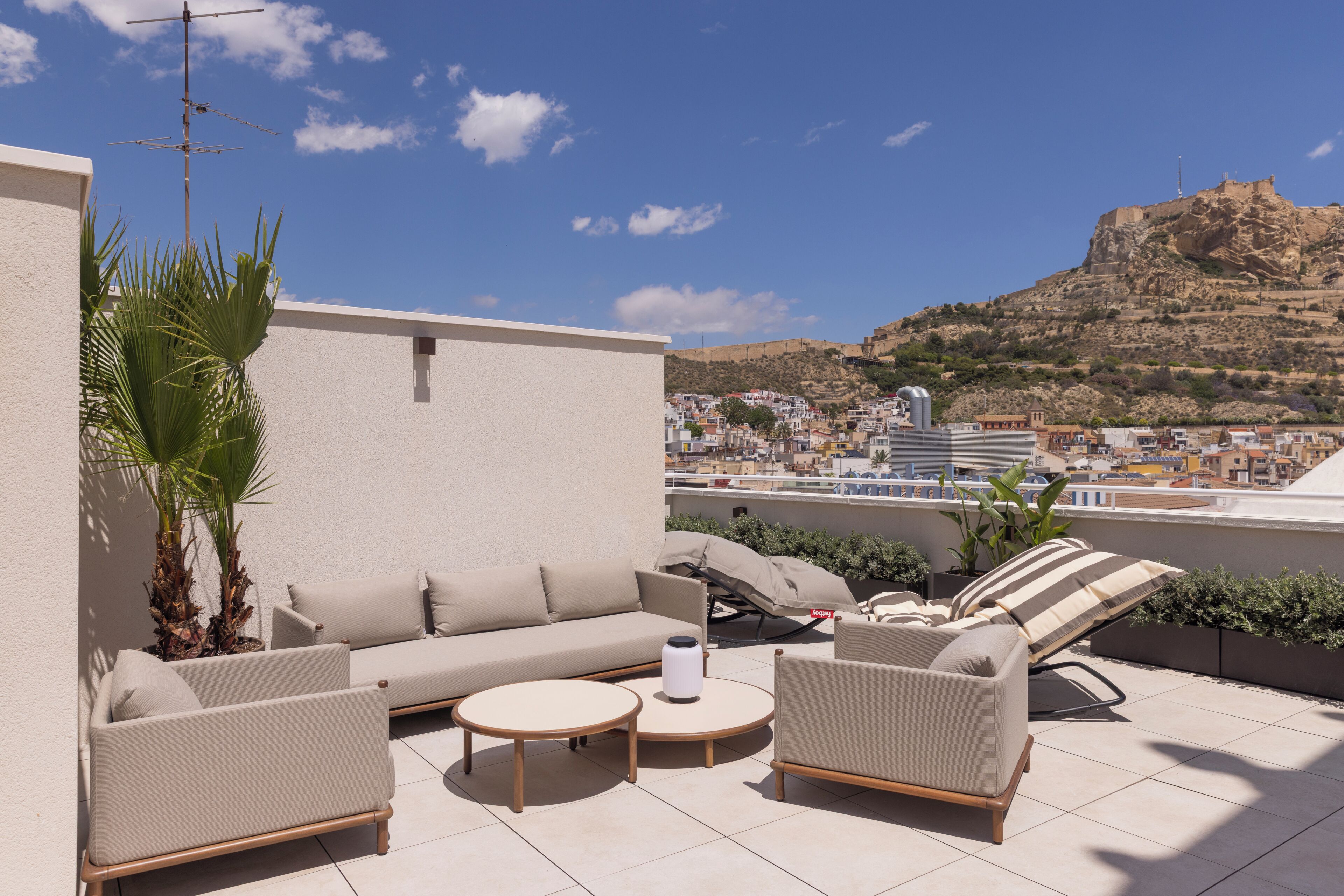 Eine Dachterrasse mit einer Couch, Stühlen und einem Tisch, mit Blick auf eine Stadtlandschaft und eine Hügelkulisse.