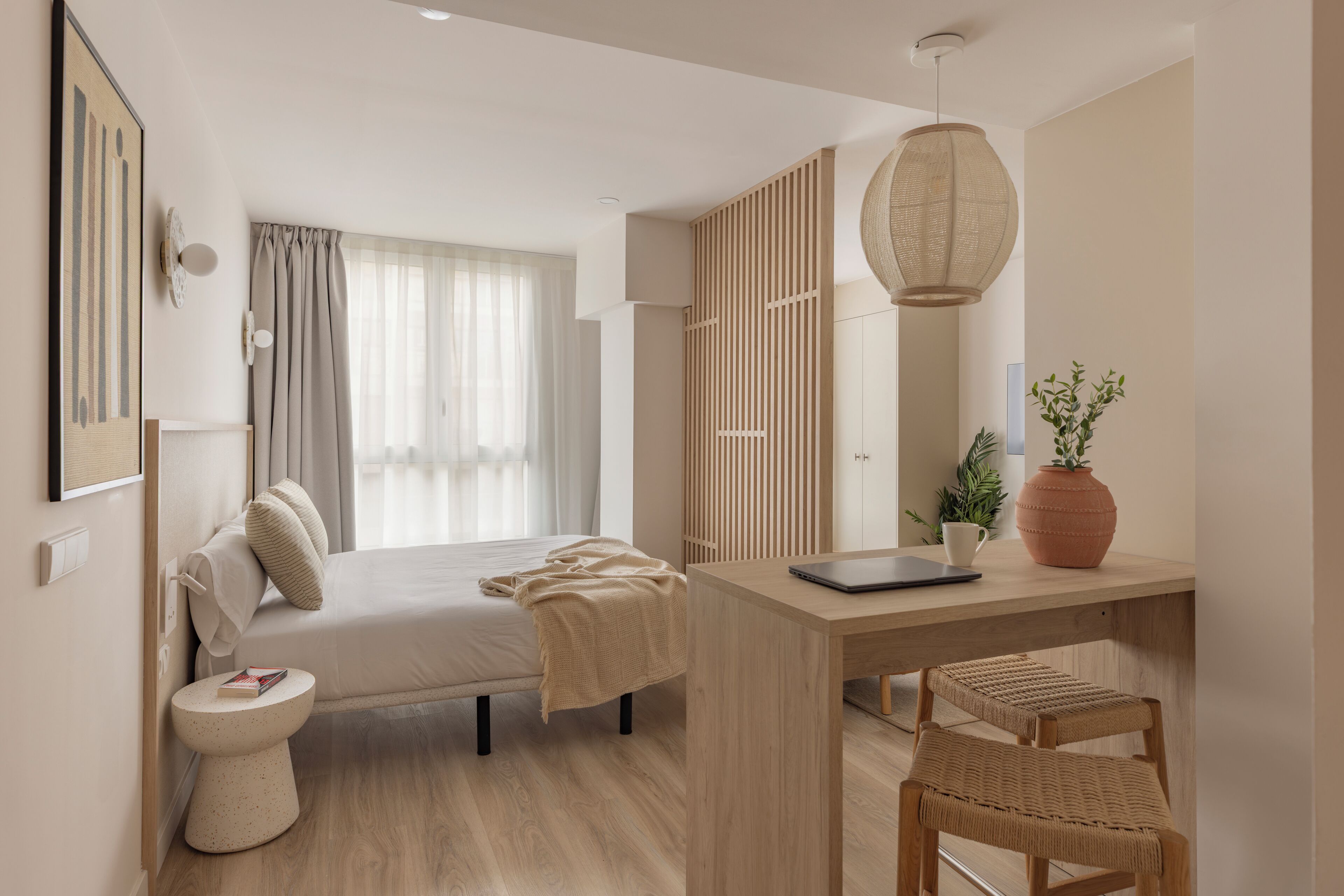 A modern bedroom with a bed, bedside table, lamp, and a view of the outdoors.