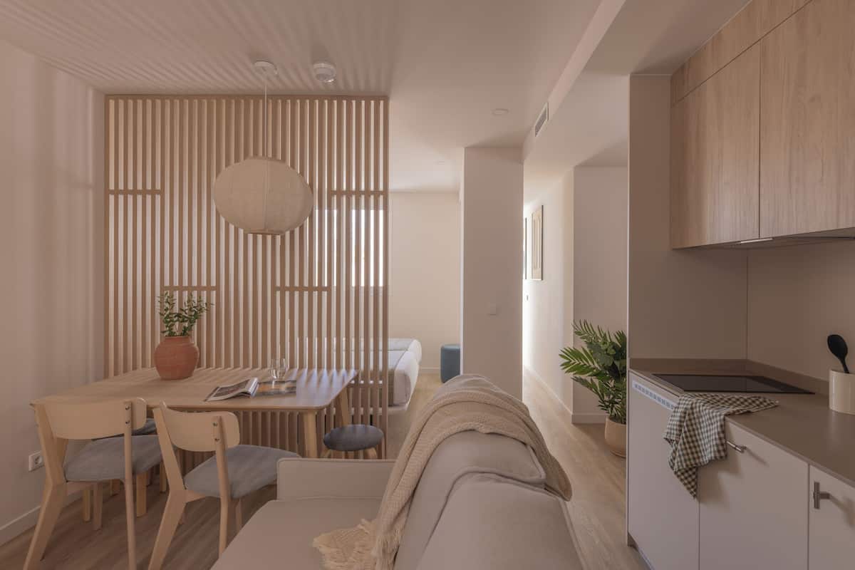 A modern kitchen with wooden cabinets, a dining area with a table and chairs, and a living area with a sofa and a potted plant.