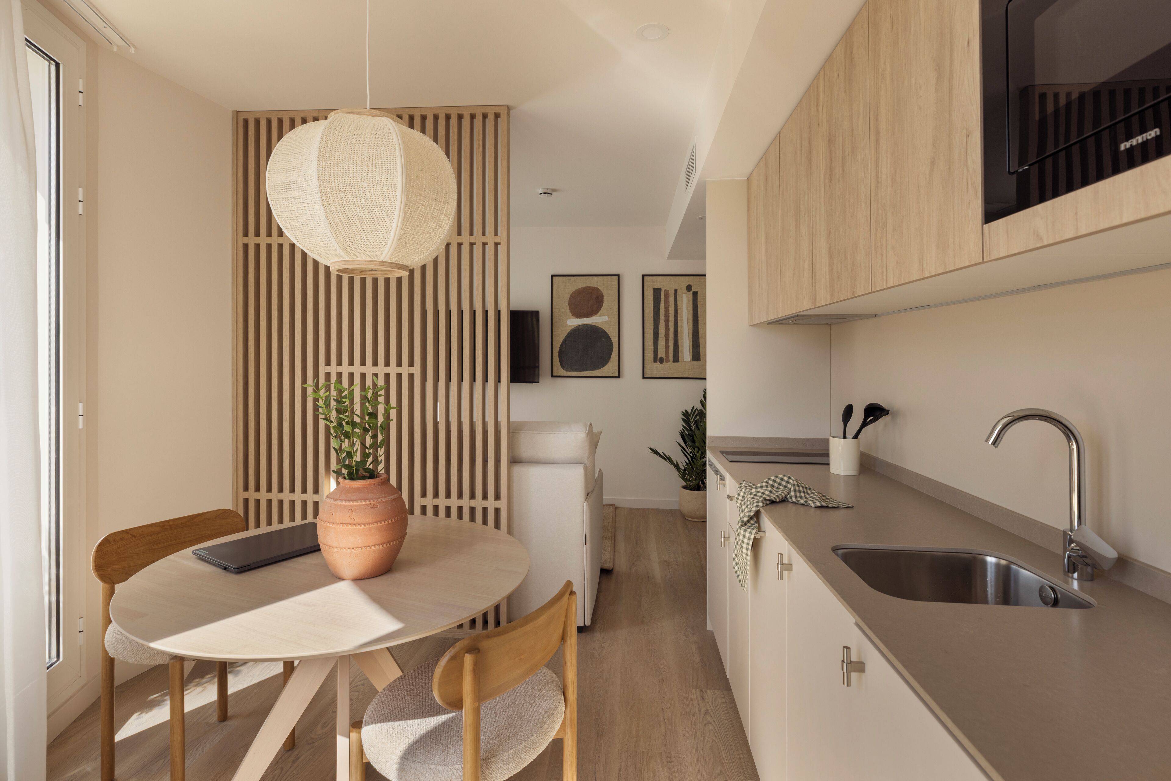 Una cocina moderna con comedor, armarios de madera, una lámpara colgante y una planta en maceta.