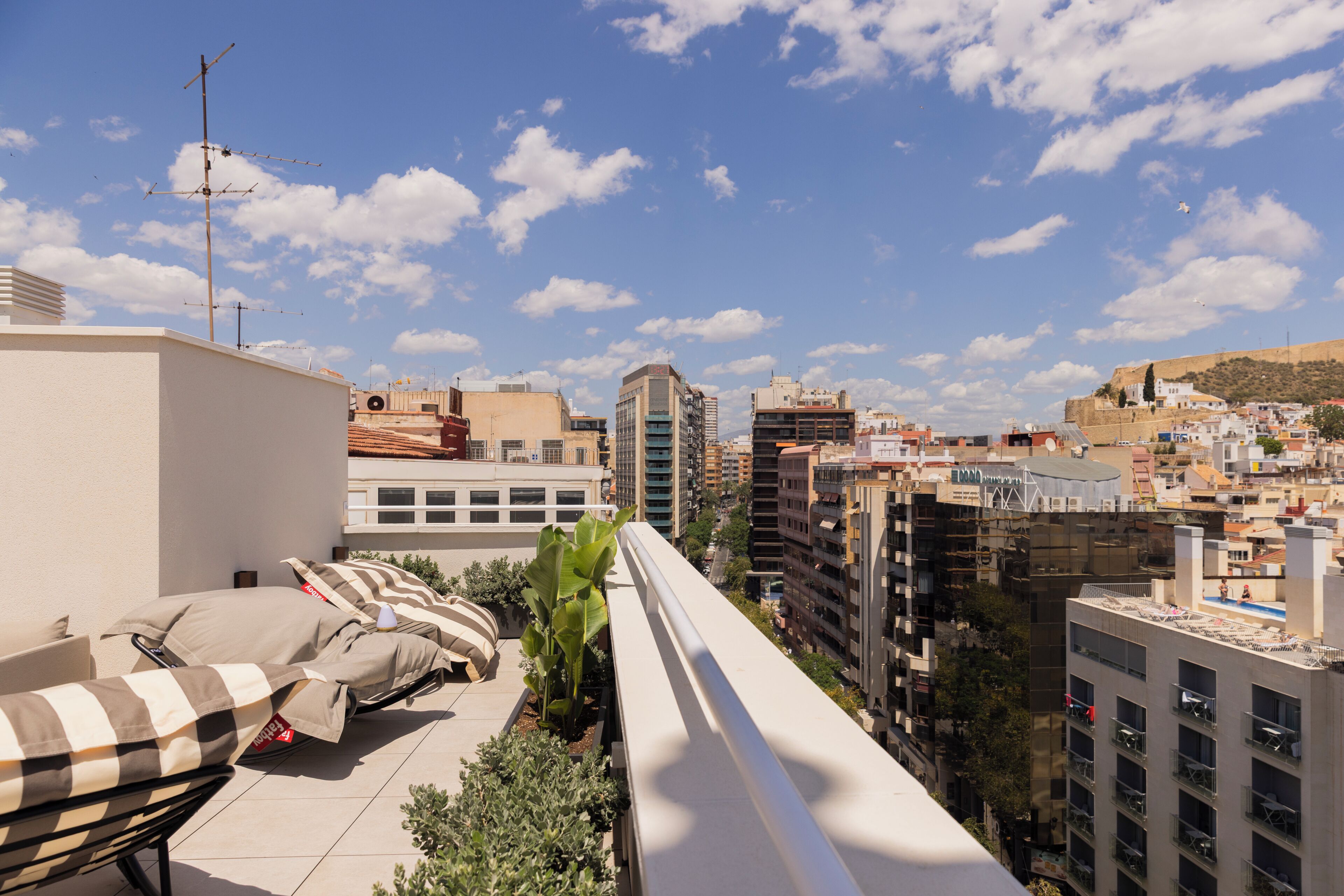 Terraza en la azotea con mobiliario exterior, vistas panorámicas de la ciudad y cielo despejado.