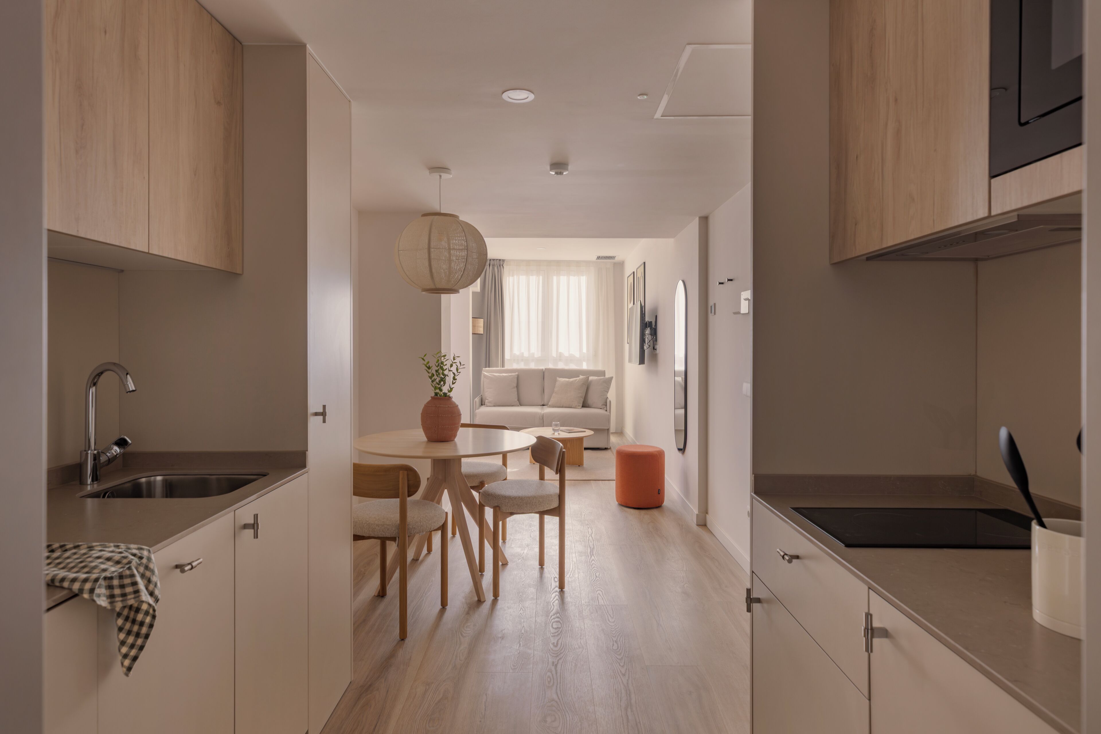 Een moderne keuken met houten kastjes, een eethoek met een ronde tafel en stoelen, en een lichtgekleurde vloer.