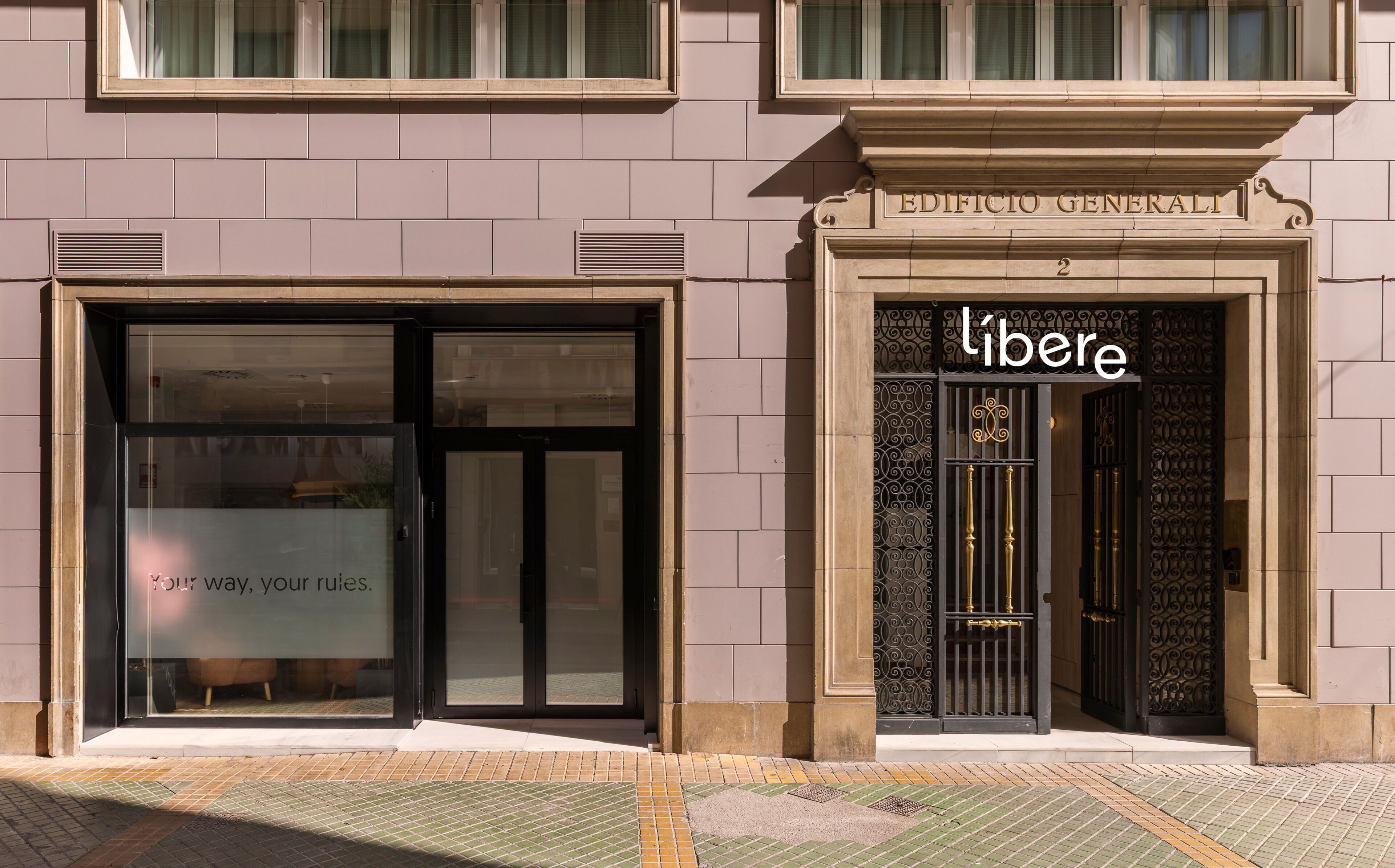 Une façade d’immeuble avec une grande entrée en verre et un portail en métal noir sur lequel est inscrit le mot « libere ».
