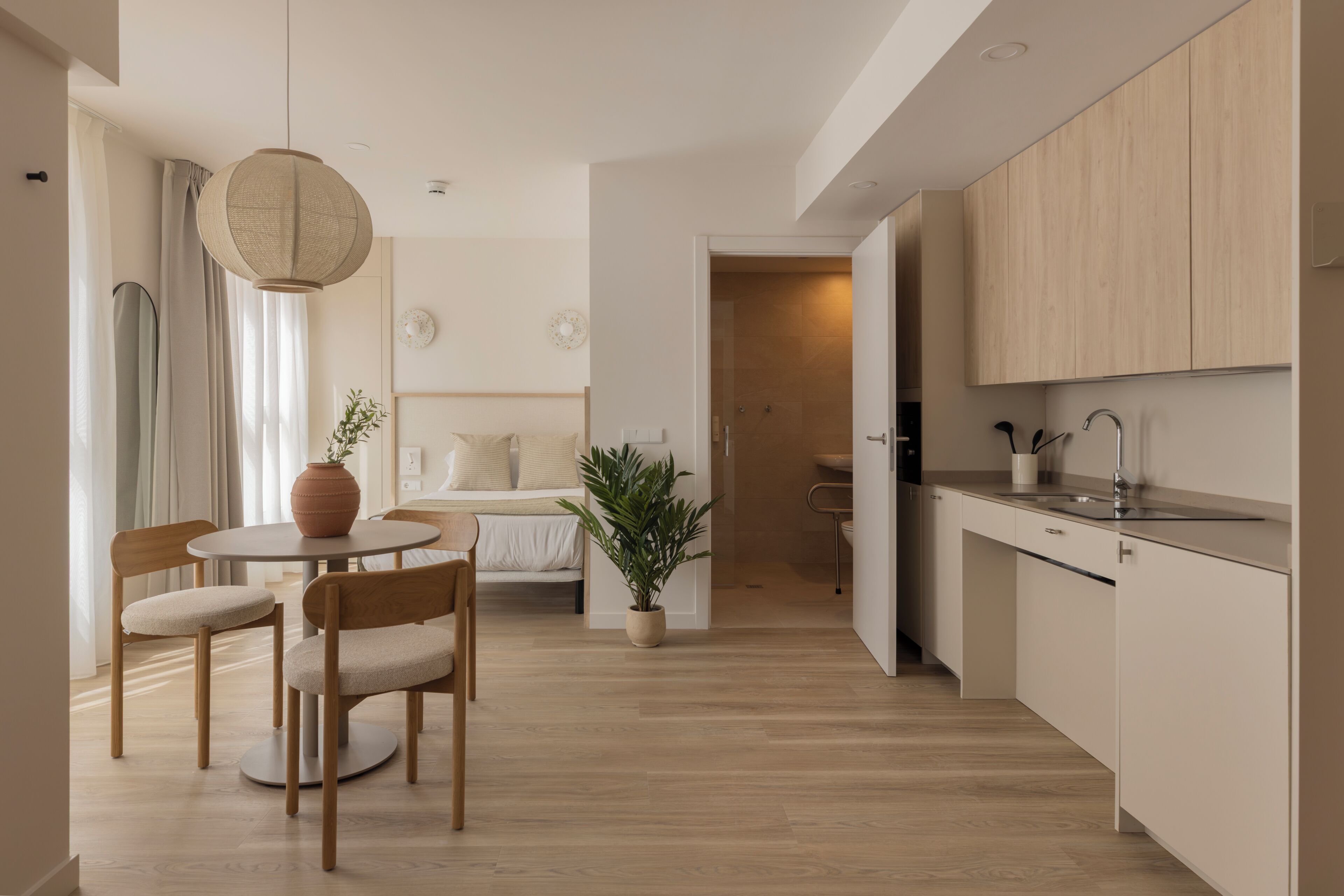 A modern kitchen with wooden cabinets, a dining area with a round table and chairs, and a visible plant.