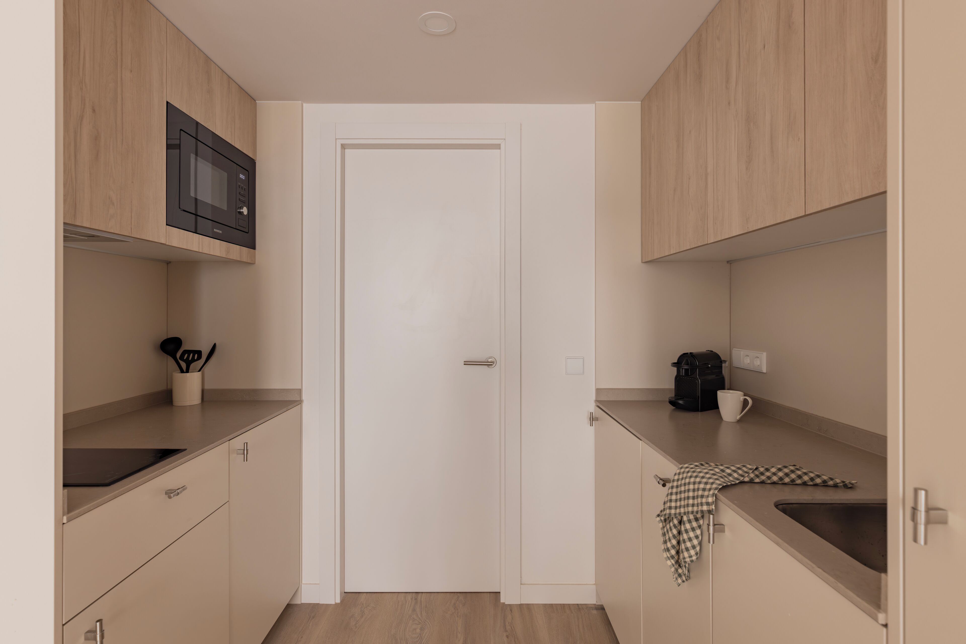 Una cocina compacta con armarios de madera, microondas, cafetera y lavabo.