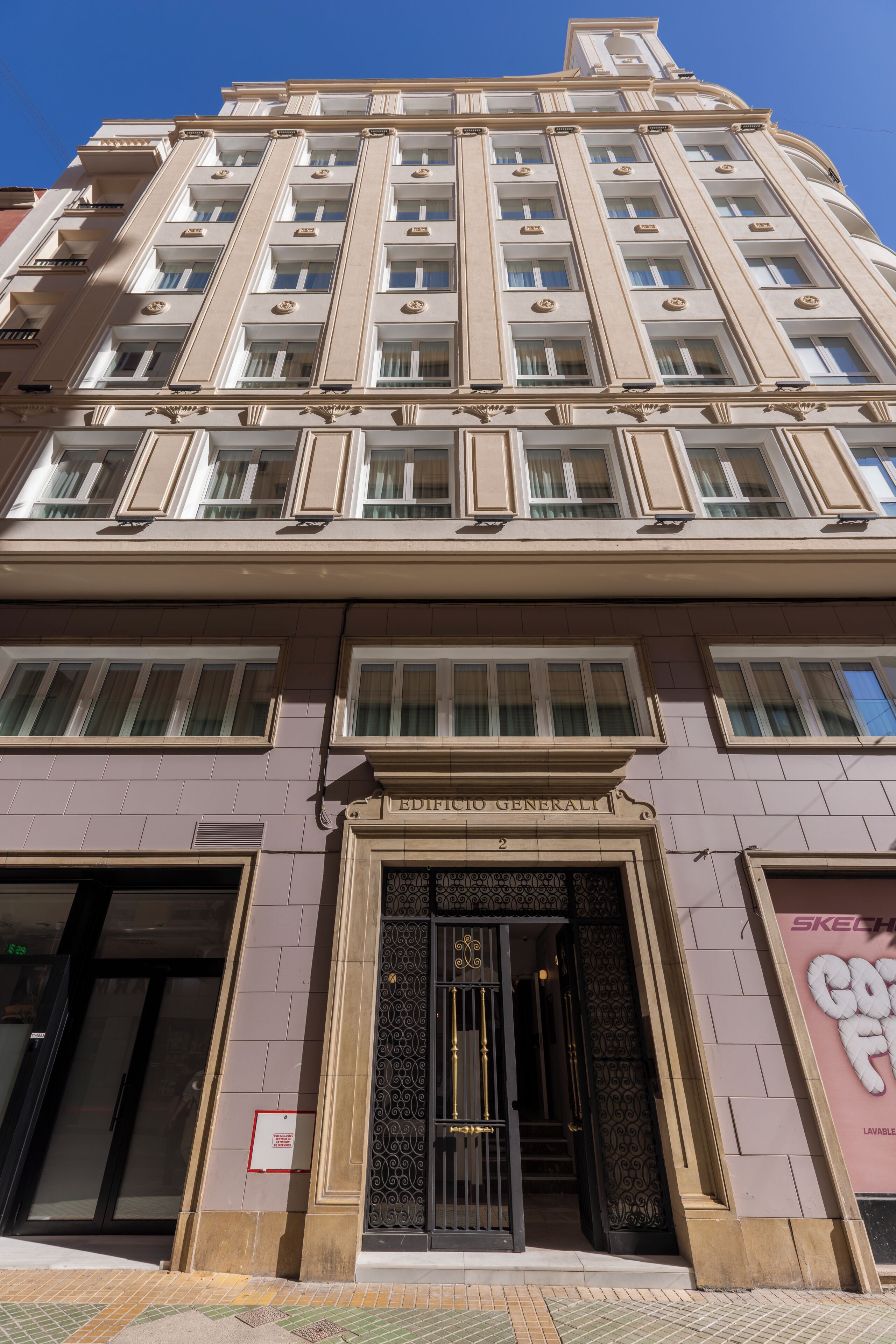 Un edificio de varios pisos con una entrada central, ventanas grandes y un cartel que indica 'EDIFICCI GENERALI'.