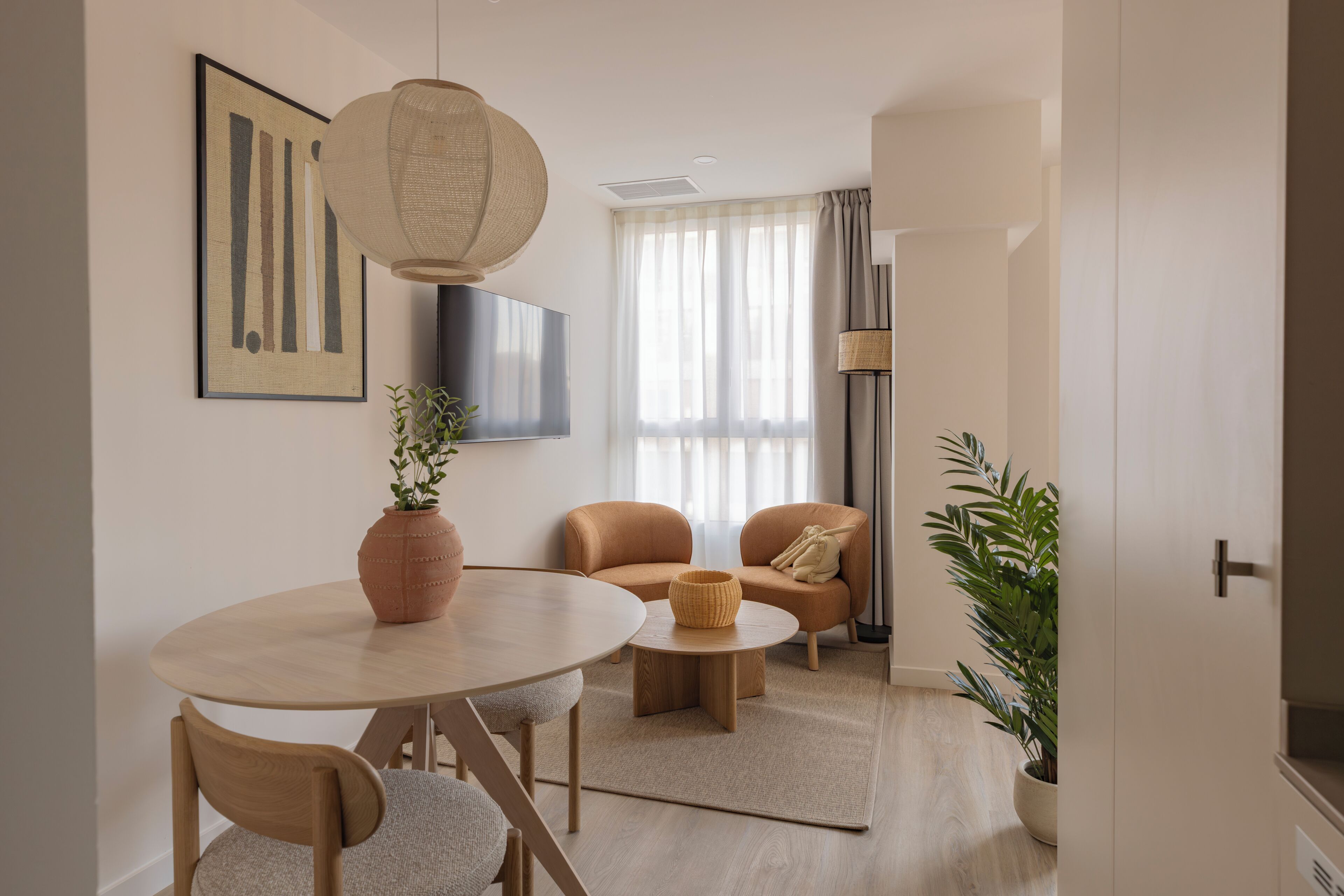 A modern living room with a round table, two sofas, a TV, and a large window with sheer curtains.