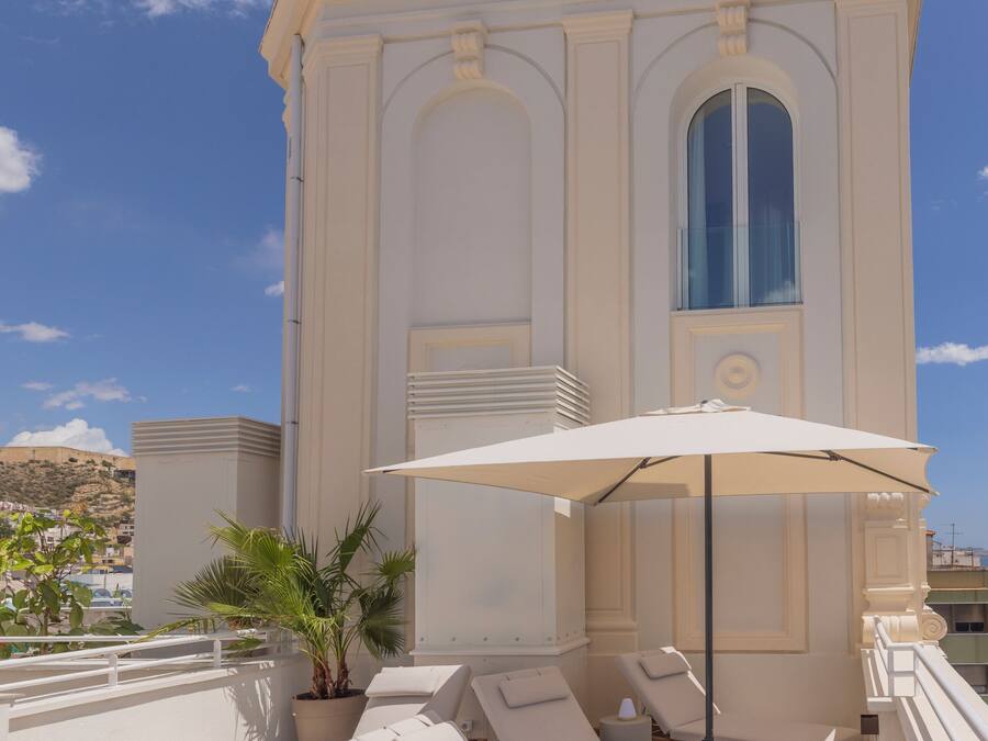 A rooftop terrace with sun loungers, a large umbrella, and a decorative building in the background.