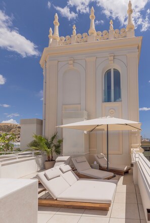 A rooftop terrace with sun loungers, a large umbrella, and a decorative building in the background. - Libere Alicante Rambla (Alicante)