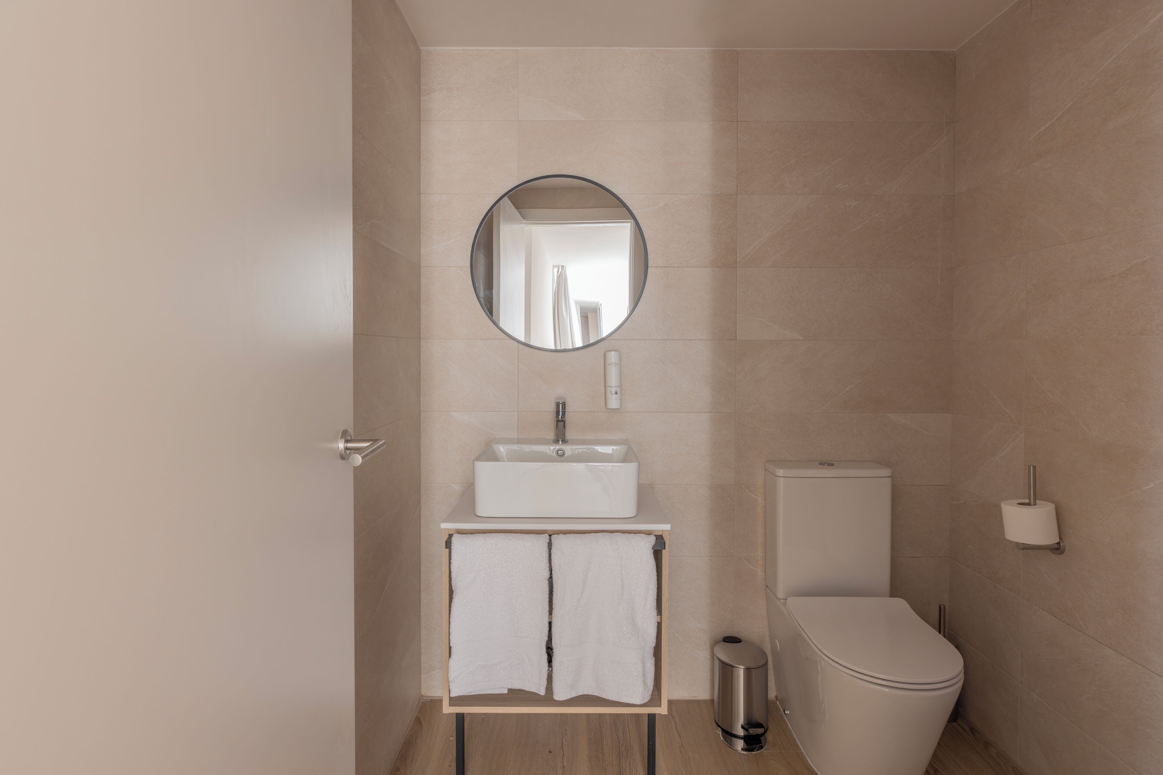 A modern bathroom with a sink, mirror, toilet, and a trash bin.