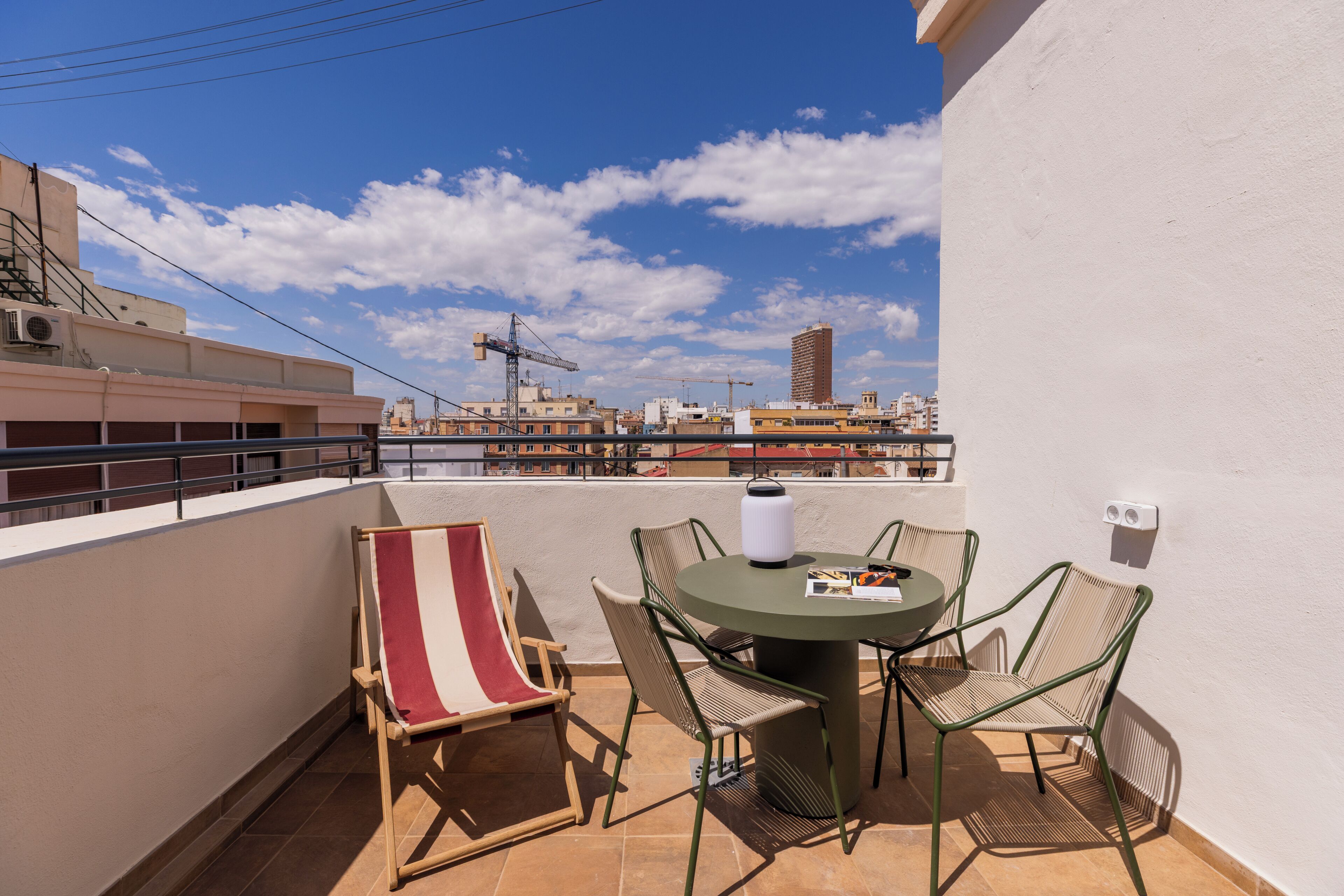 A balcony with a table and chairs, a striped beach chair, and a view of the cityscape.