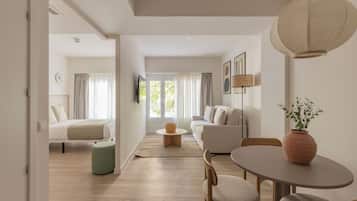 A modern hotel room with a bed, sofa, dining table, and a view of the outdoors.