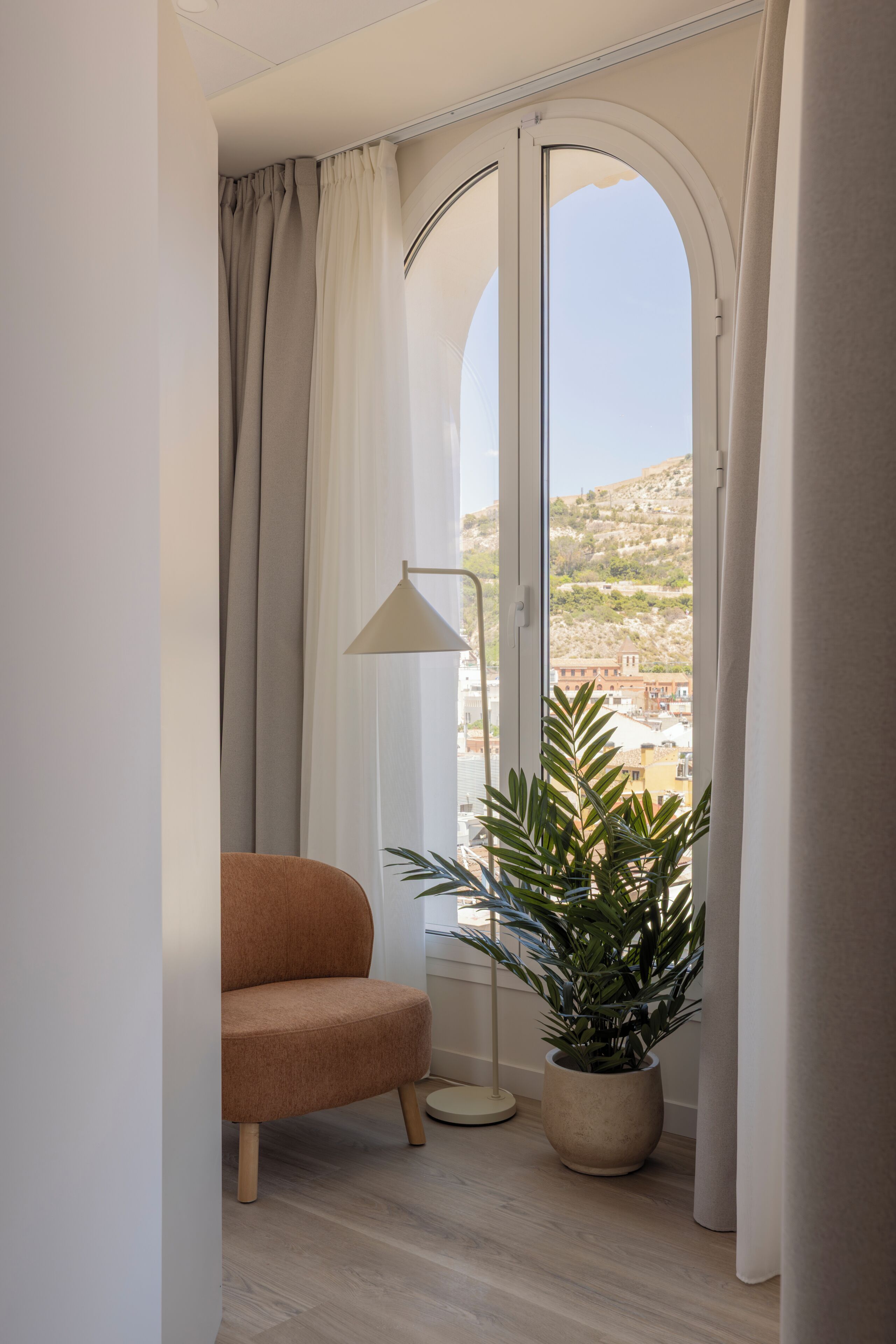 Una habitació amb un finestral gran d'arc, una planta en test, una làmpada de peu i un sofà.