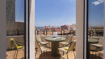 Un balcón con una mesa redonda y sillas, con vistas a un paisaje urbano que incluye edificios y un cielo despejado.