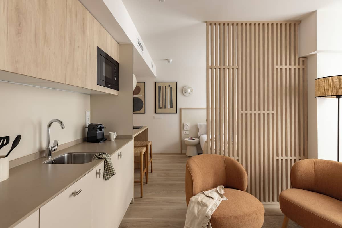 A modern kitchen with a built-in microwave, a sink, and a coffee machine. There is a dining area with a table and chairs, and a sliding door leading to a bathroom.