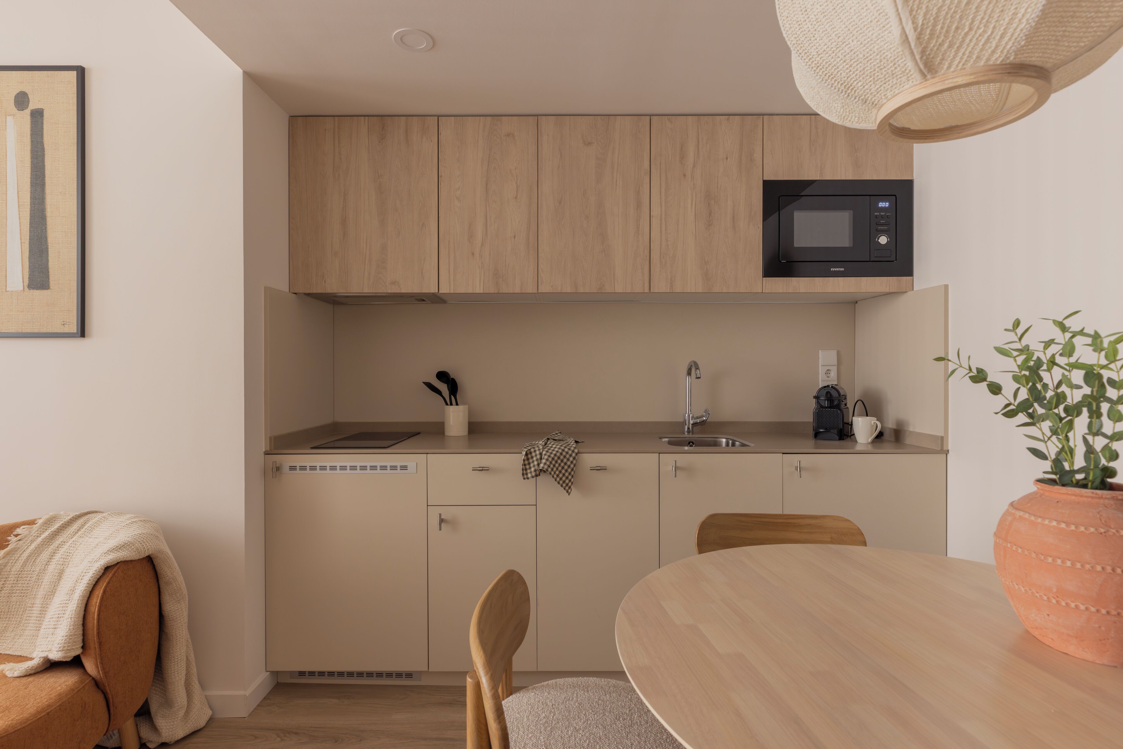 A modern kitchen with wooden cabinets, a microwave, a sink, and a dining area with a table and chairs.