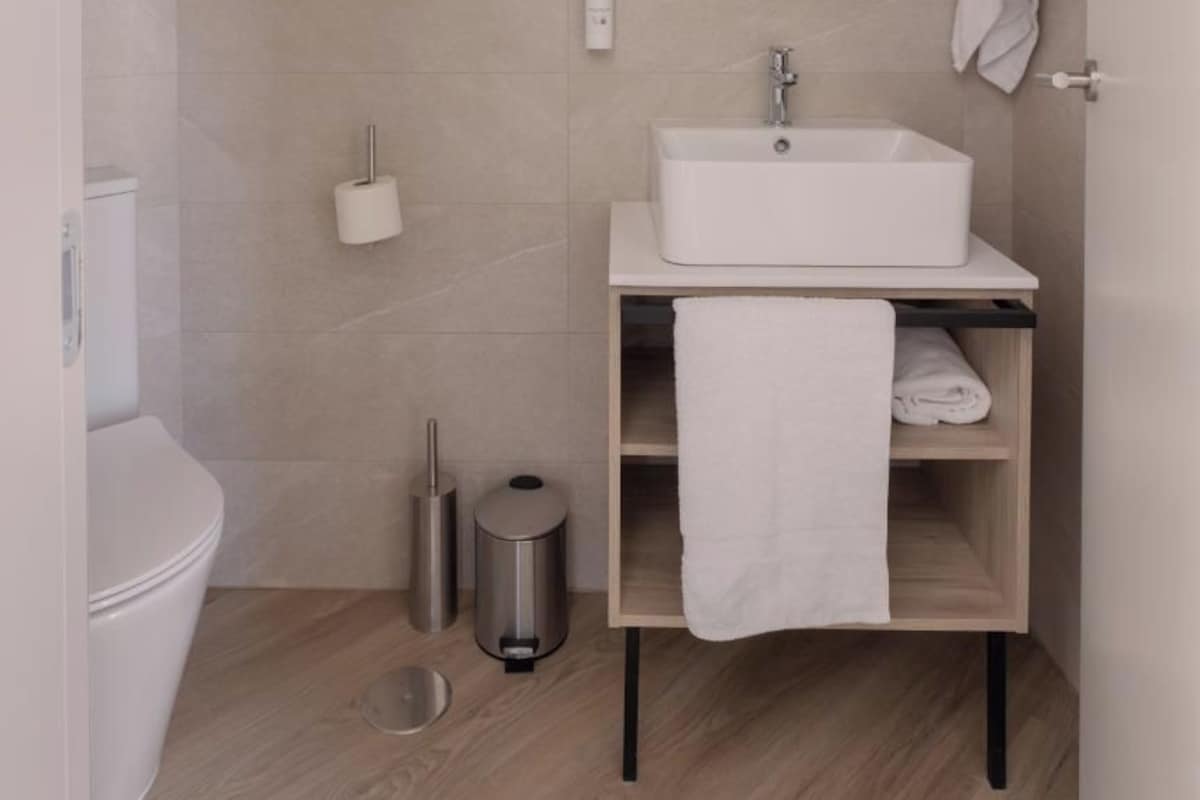 A modern bathroom with a white sink, round mirror, and a towel rack.