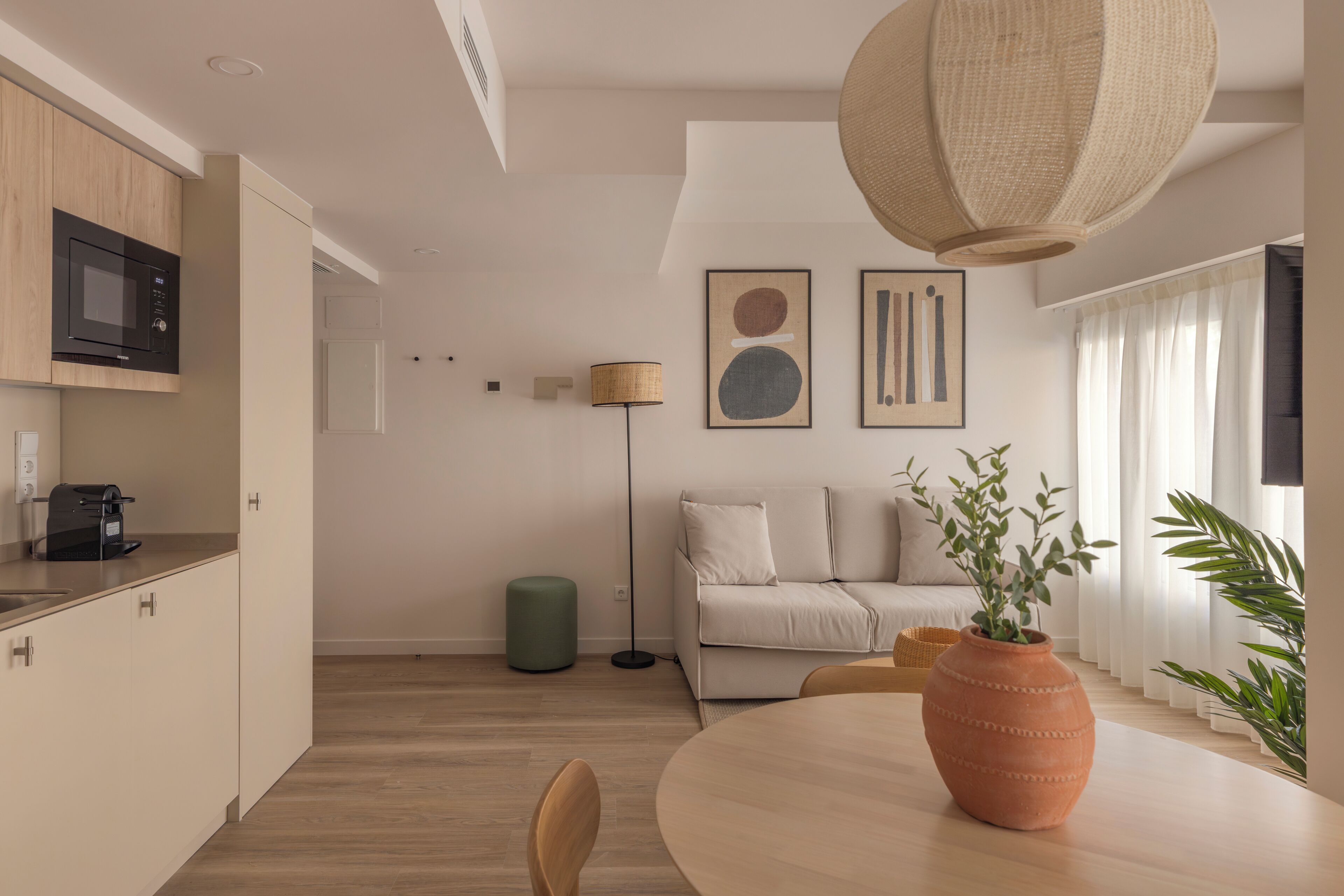 A modern kitchen with a microwave, a dining table with chairs, a green ottoman, and a large woven light fixture.