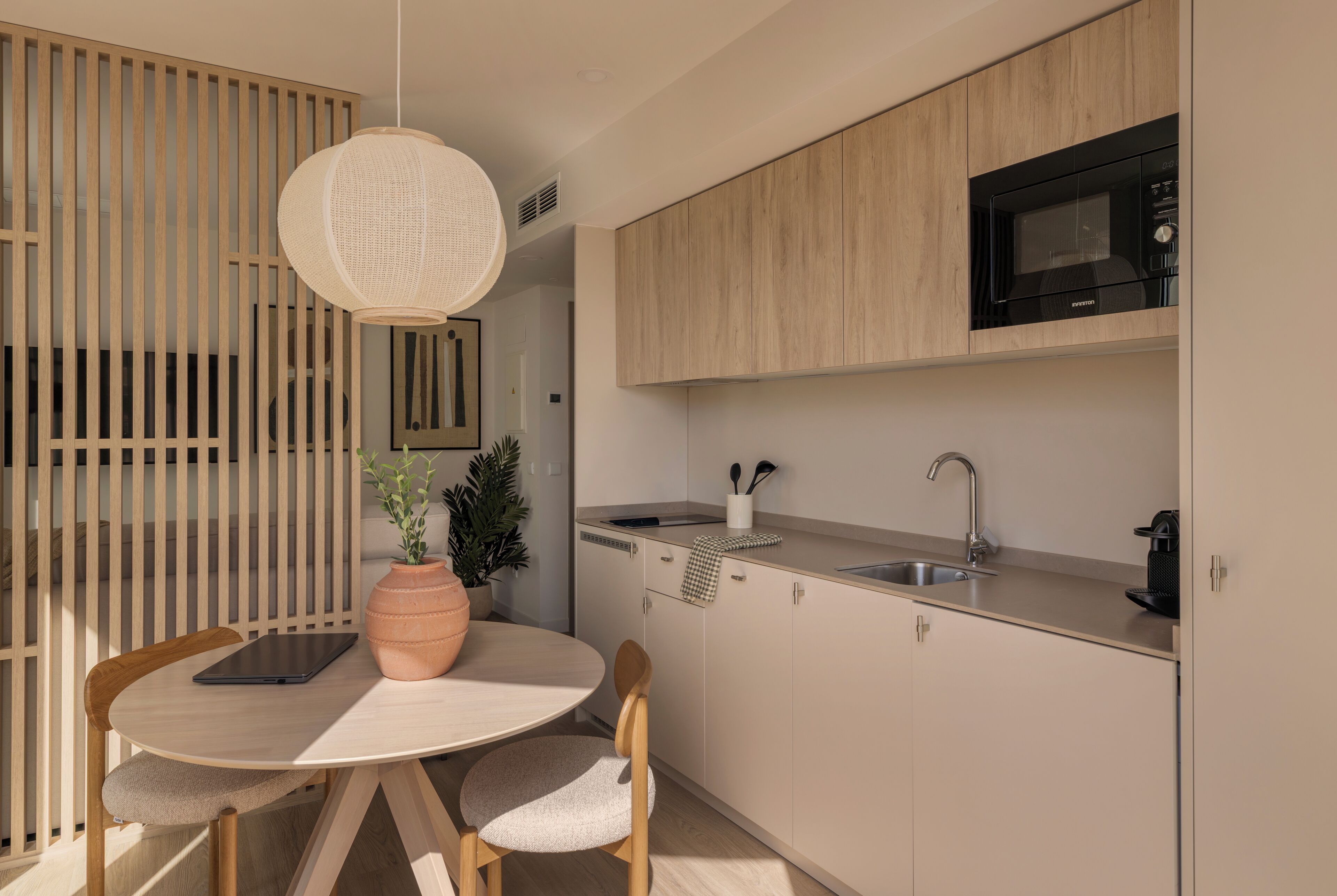 A modern kitchen with a round dining table, wooden chairs, a hanging light fixture, and a built-in microwave.